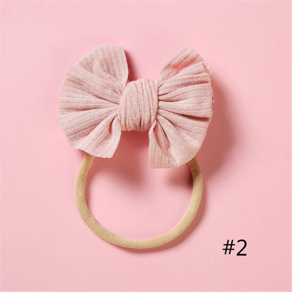 A pink knitted bow headband with a soft elastic band displayed on a light pink background.