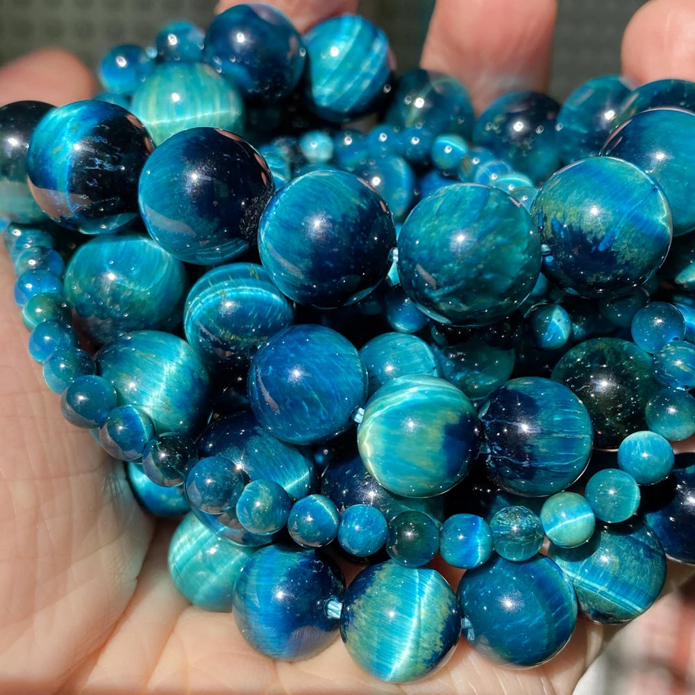 A handful of polished blue and green gemstone beads, including tiger eye and lava, held in a person's hand.