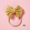 A golden yellow ribbed fabric bow headband with a soft elastic band against a pink background.