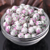 A clear glass bowl filled with small white ceramic beads decorated with pink floral patterns.
