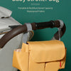 A yellow portable baby stroller bag with multiple compartments is shown attached to a stroller handlebar.