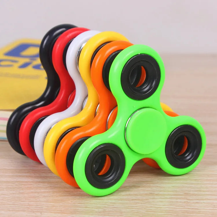 A set of colorful ABS tri-spinner fidget toys stacked together on a wooden surface.