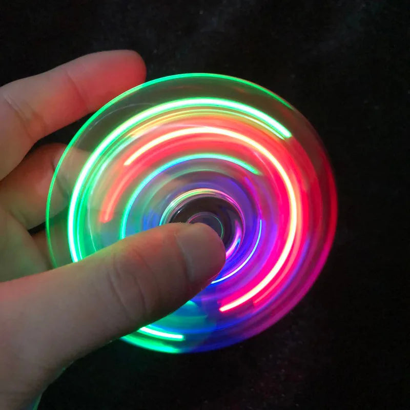 A hand holds a glowing, multi-colored LED fidget spinner, displaying vibrant light rings.