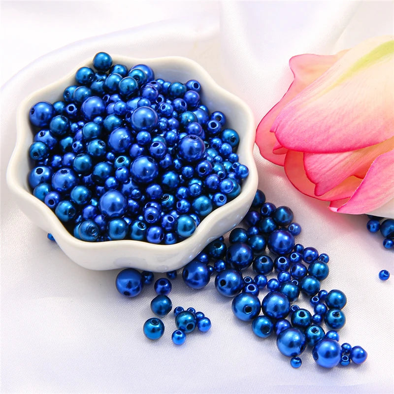 A pile of assorted blue pearl beads for jewelry making next to a pink lotus flower.