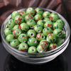 A bowl filled with small, round ceramic beads featuring floral patterns in green and reddish-brown colors.