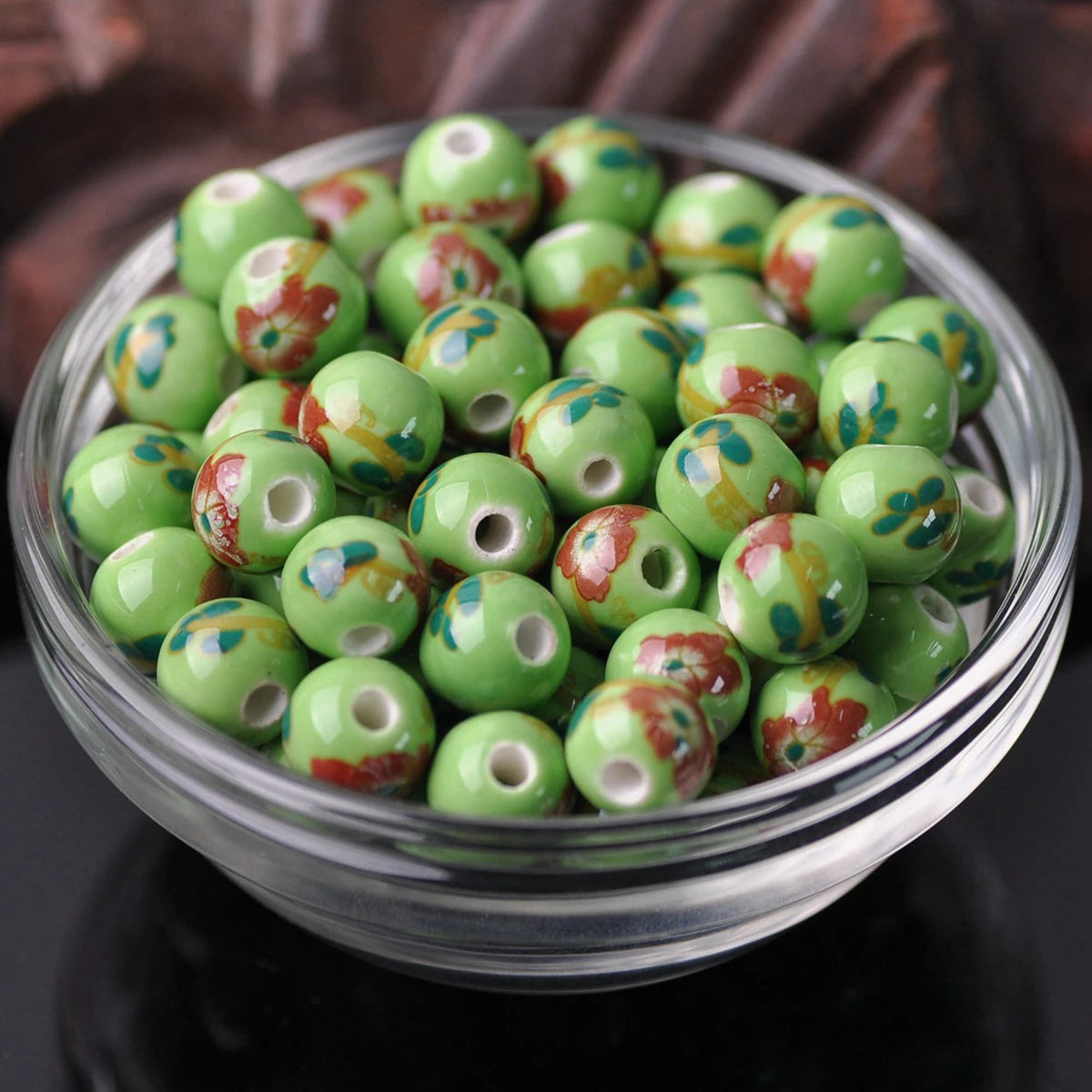 A bowl filled with small, round ceramic beads featuring floral patterns in green and reddish-brown colors.
