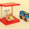 A wooden train track accessory set featuring an airport and gas station scene with a red platform and a blue train.