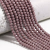 A strand of small, faceted pink crystal glass beads laid out on a white surface.