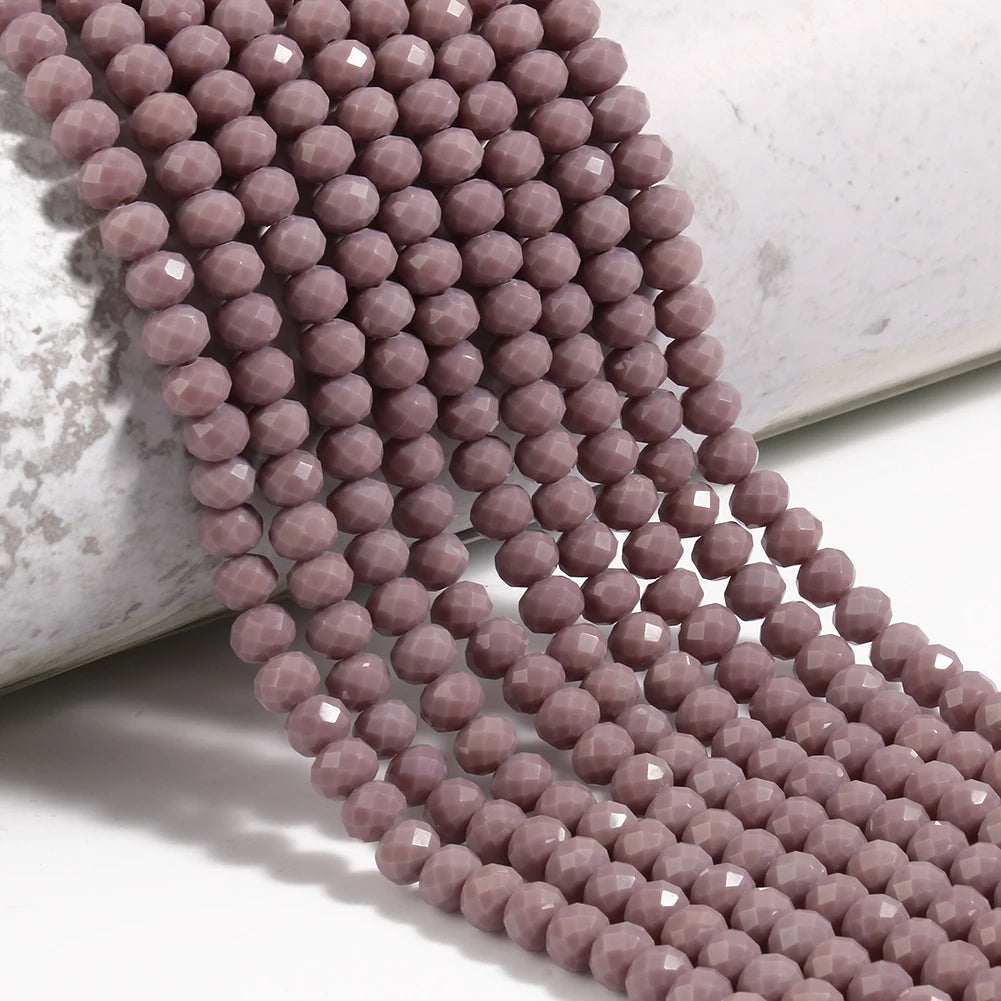 A strand of small, faceted pink crystal glass beads laid out on a white surface.