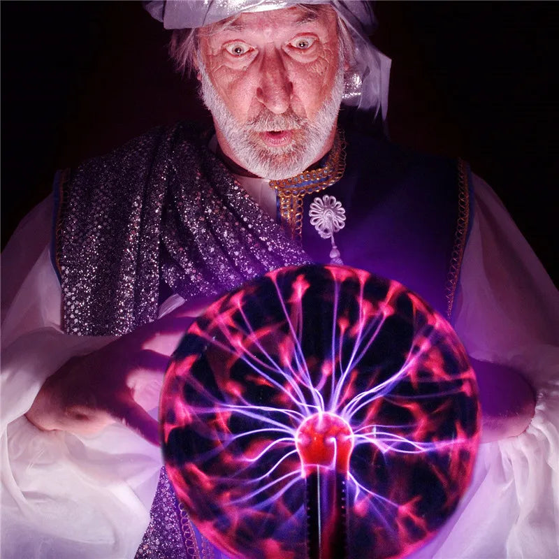 An elderly man with a white beard is holding a glowing plasma ball lamp in his hands.