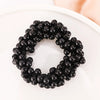 A circular arrangement of black pearl hair ties with bows, displayed on a white plate.