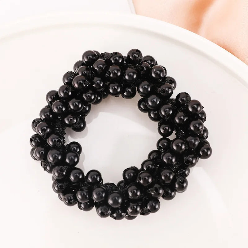 A circular arrangement of black pearl hair ties with bows, displayed on a white plate.