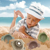 A toddler is playing in sand with a set of boat-shaped stacking cups and bath toys.