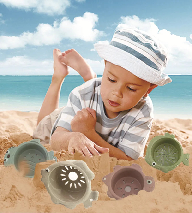 A toddler is playing in sand with a set of boat-shaped stacking cups and bath toys.
