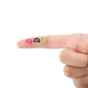 A hand holds three colorful metal open jump rings: pink, black, and green.