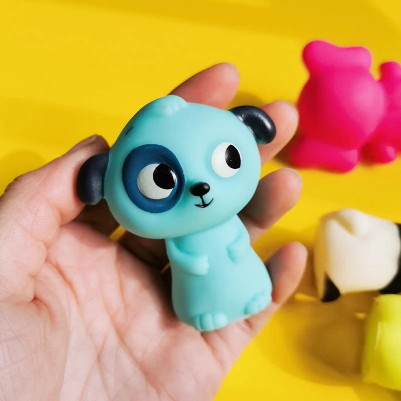 A hand holds a light blue animal finger puppet with large eyes and black ears against a bright yellow background.