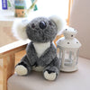 A gray koala plush toy with white fur and black accents sitting next to a white glass lantern.