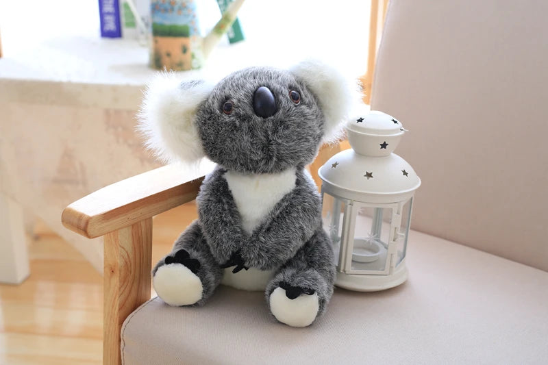A gray koala plush toy with white fur and black accents sitting next to a white glass lantern.