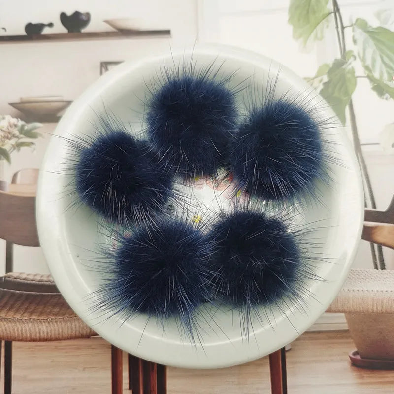 A collection of dark blue and black mink fur pom poms displayed on a white plate.