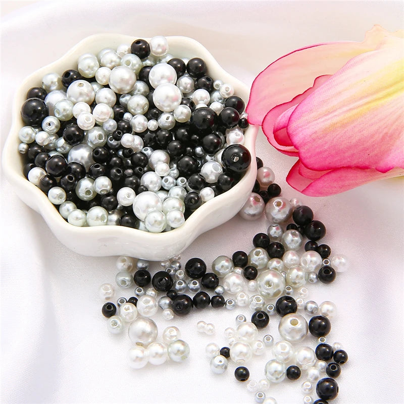 A white bowl filled with an assortment of black and white pearl beads, some loose on the surface.