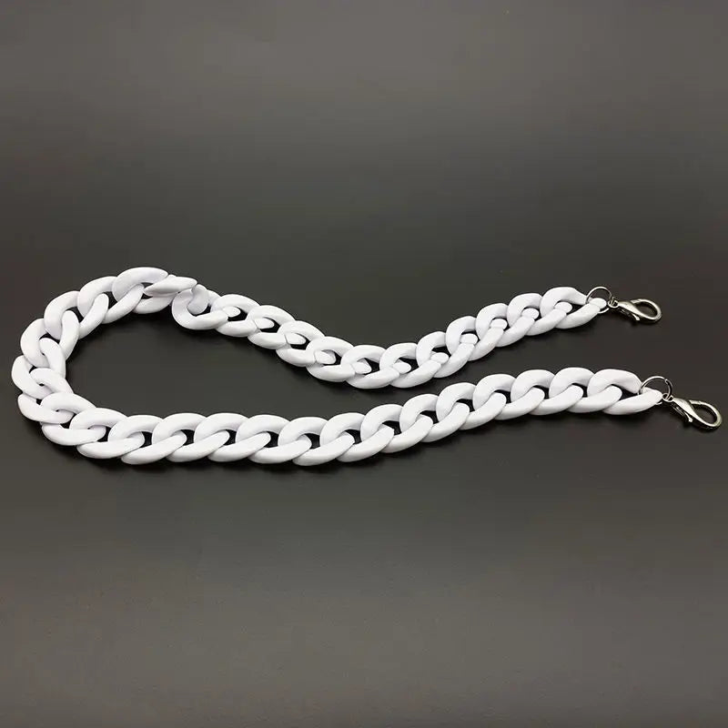 A silver-toned acrylic bag chain strap with links and clips laid out on a dark gray surface.