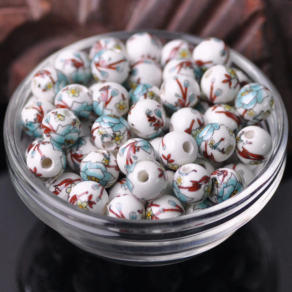 A clear glass bowl filled with small white ceramic beads decorated with blue and red floral patterns.