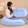 A light blue Rimuru Tempest plush toy pillow with closed eyes and rosy cheeks is resting on a person's lap.