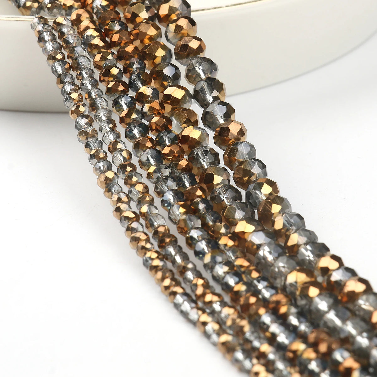 A close-up of multiple strands of faceted crystal glass beads in gold and gray tones for jewelry making.