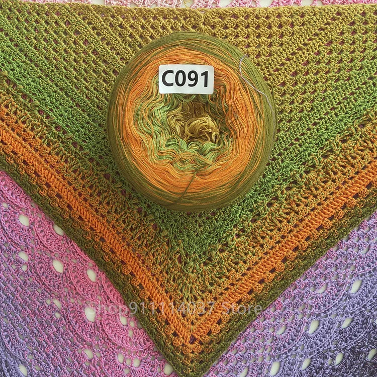A ball of rainbow gradient mercerized cotton cake yarn labeled C091 resting on a green knitted mat.