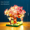 A miniature cherry tree house model featuring pink blossoms and lights on a wooden base.