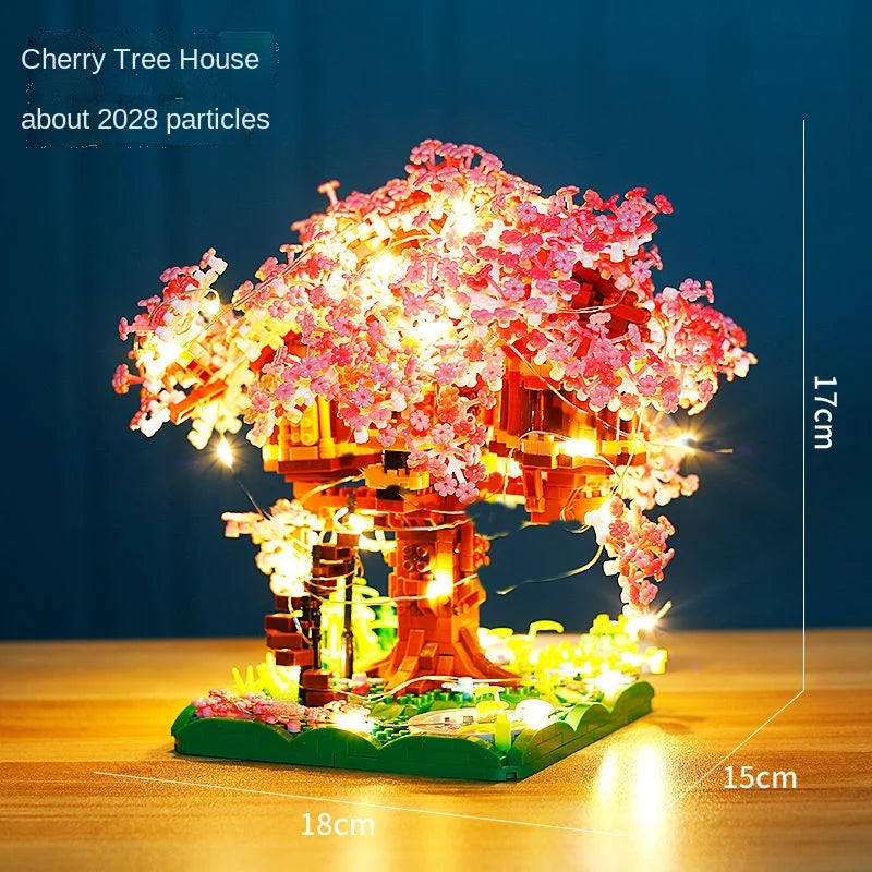 A miniature cherry tree house model featuring pink blossoms and lights on a wooden base.