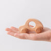 A small wooden and silicone car teether toy is held in an open human hand.