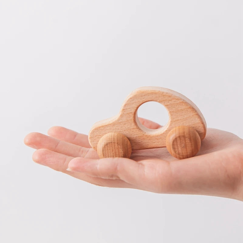 A small wooden and silicone car teether toy is held in an open human hand.