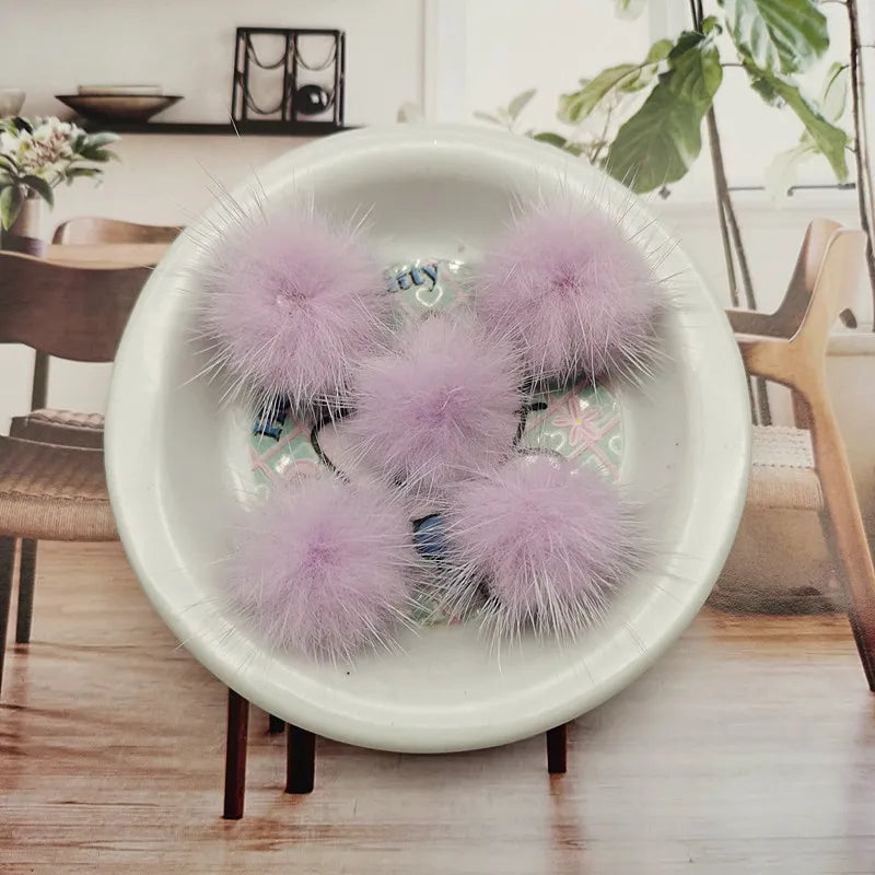 A collection of fluffy purple mink fur pom poms displayed in a white bowl on a wooden table.