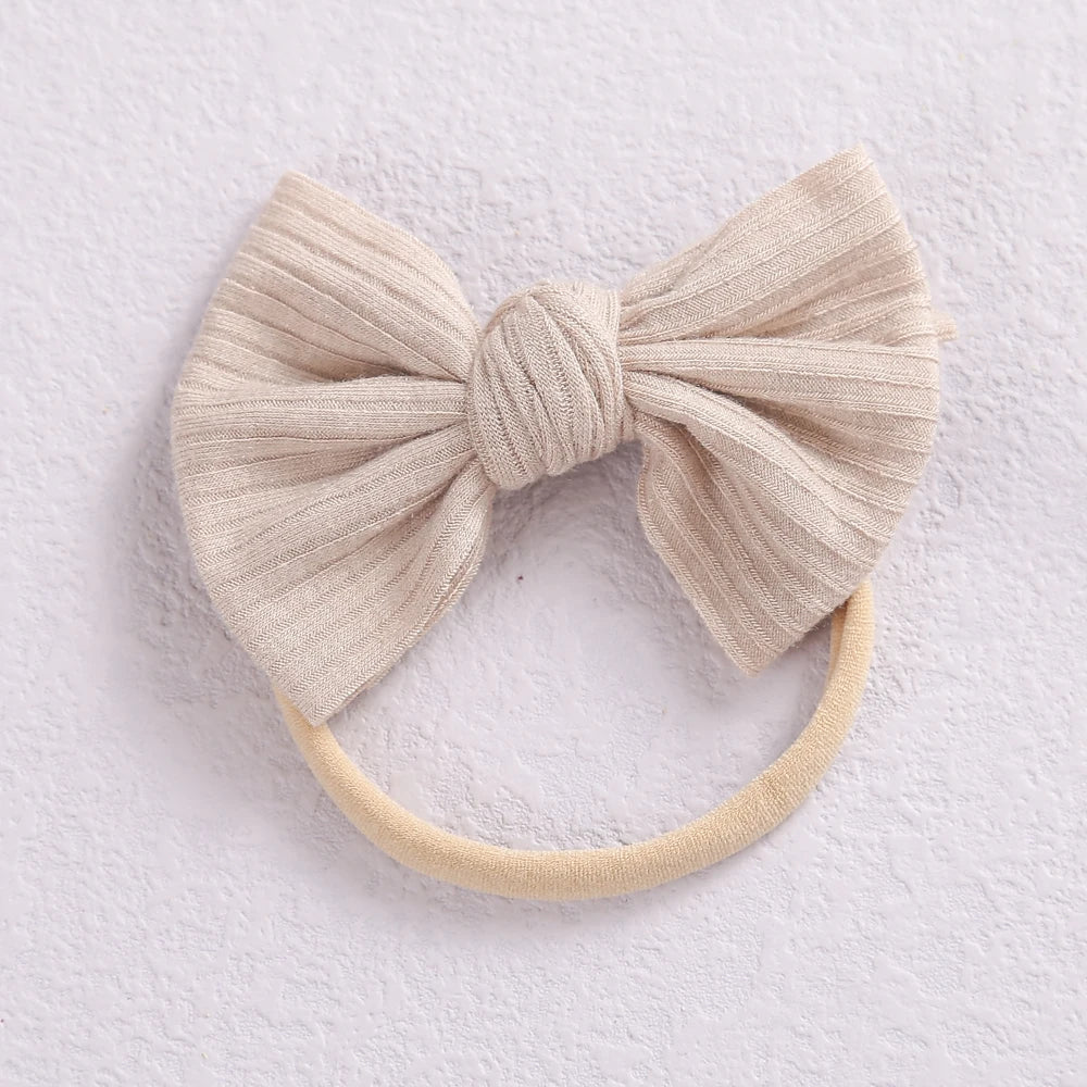 A beige fabric bow headband with a soft elastic band, shown against a white background.