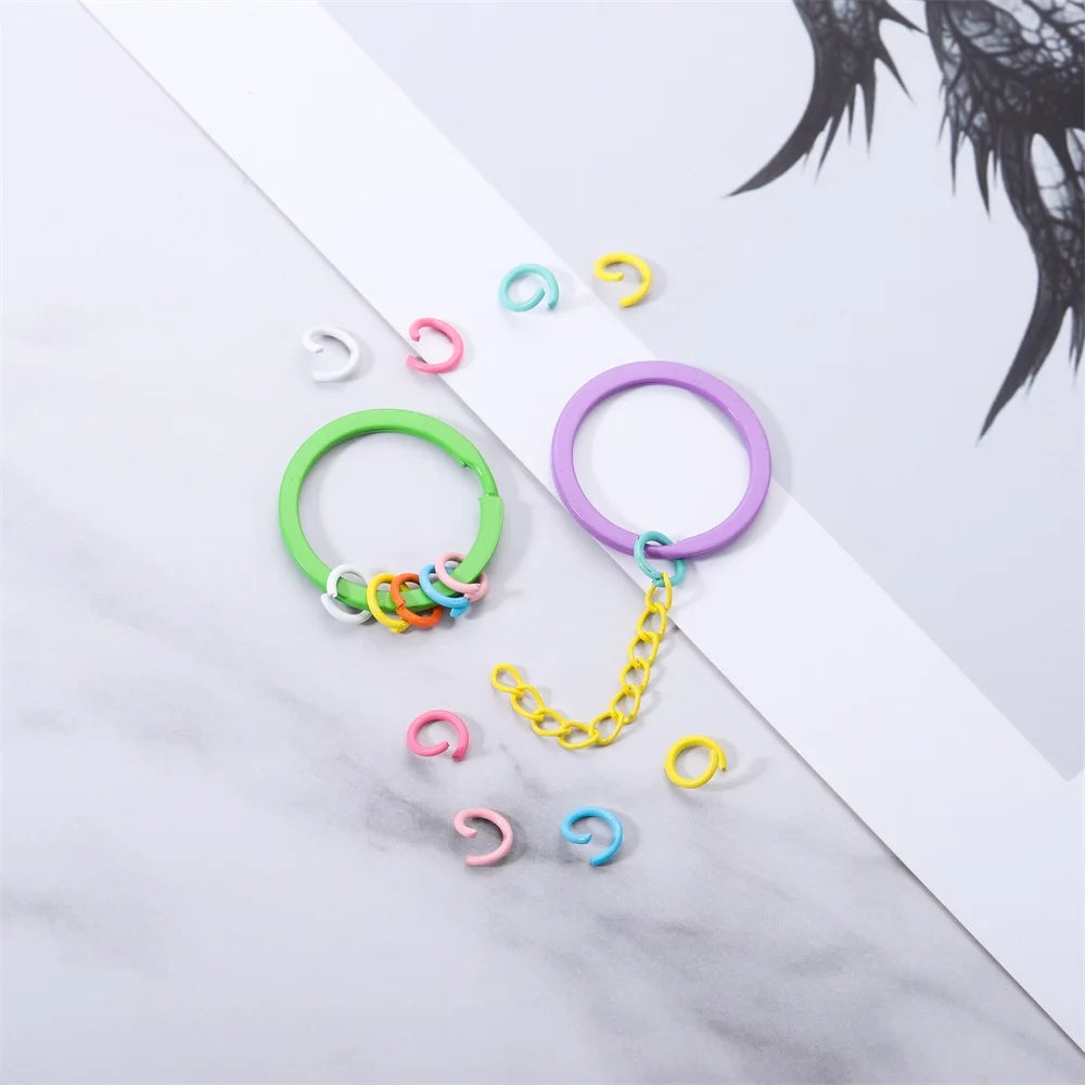 A collection of colorful metal open jump rings, including green and purple rings with attached chains, displayed on a white s