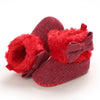 A pair of deep red knitted ankle boots with fluffy red faux fur trim and a ribbed sole.