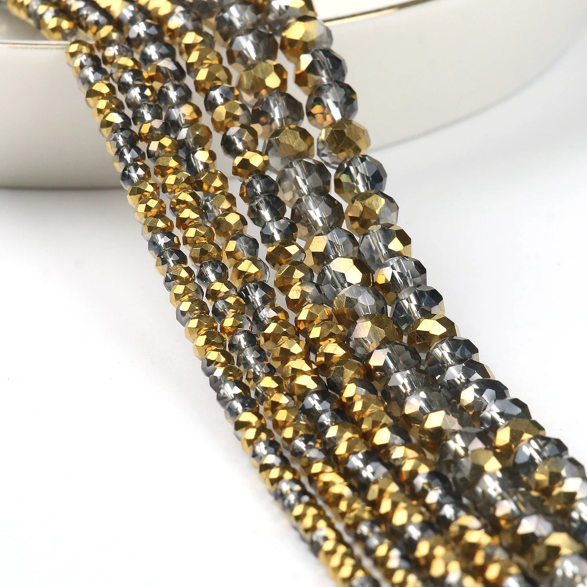 A close-up of multiple strands of faceted crystal glass beads in gold and gray tones for jewelry making