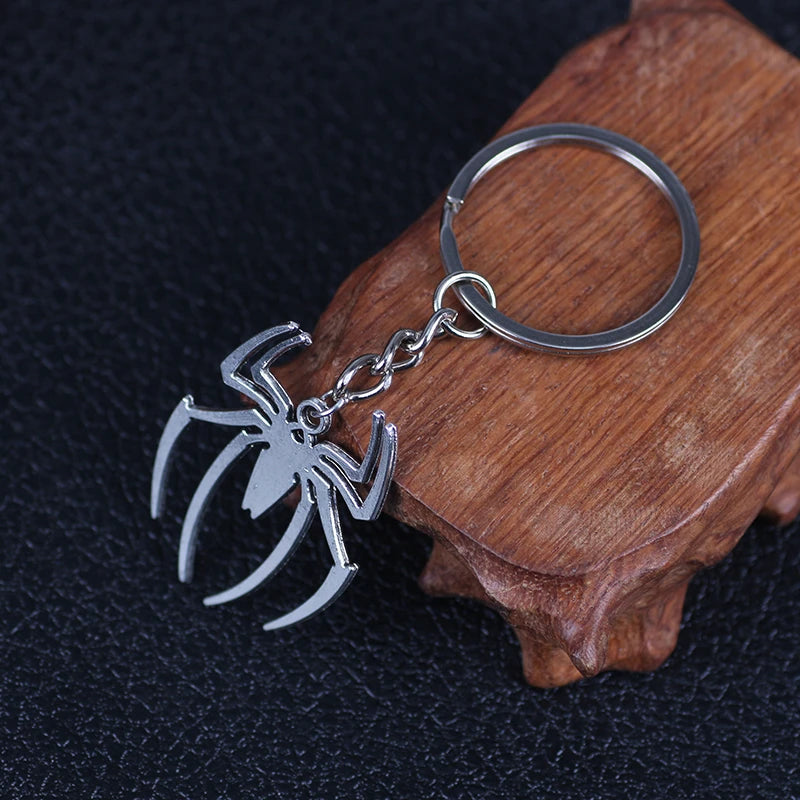 Silver spider pendant charm attached to a keyring resting on a wooden surface.