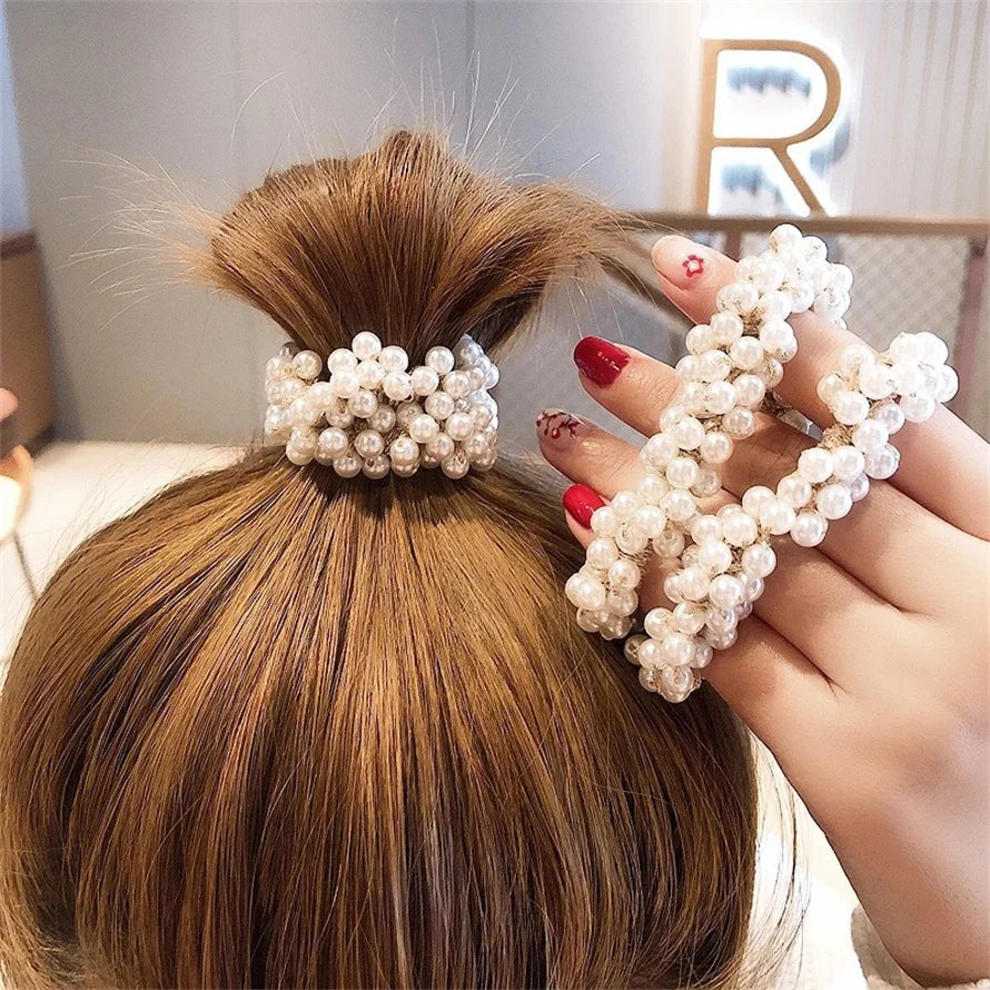 A hand is shown tying elegant pearl hair ties into a high ponytail on long brown hair.