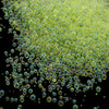 A close-up view of small, translucent green glass bubble beads scattered against a black background.