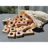 A pile of wooden gemstone building blocks with acrylic crystals is shown spilling out of a beige cloth bag.
