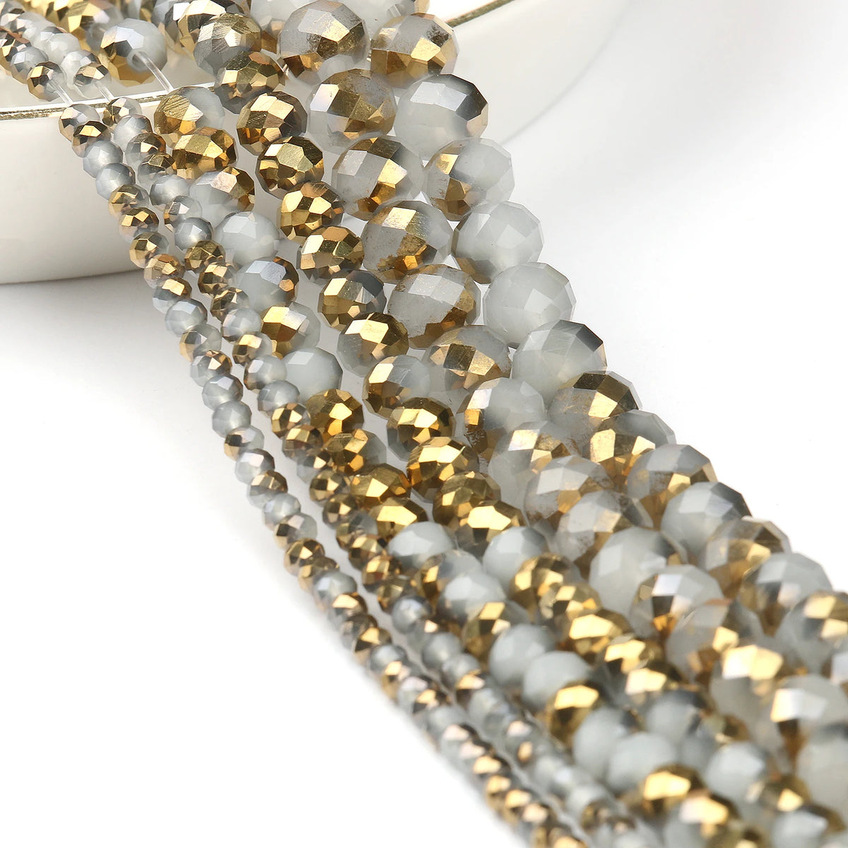 A close-up of multiple strands of faceted crystal glass beads in gray and gold tones for jewelry making