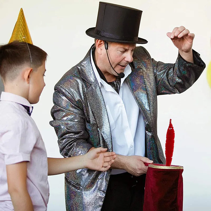 A magician in a sparkly jacket performs a trick with a red object while interacting with a young boy.