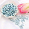 A bowl of light blue pearl beads is shown next to a pink lotus flower on white fabric.
