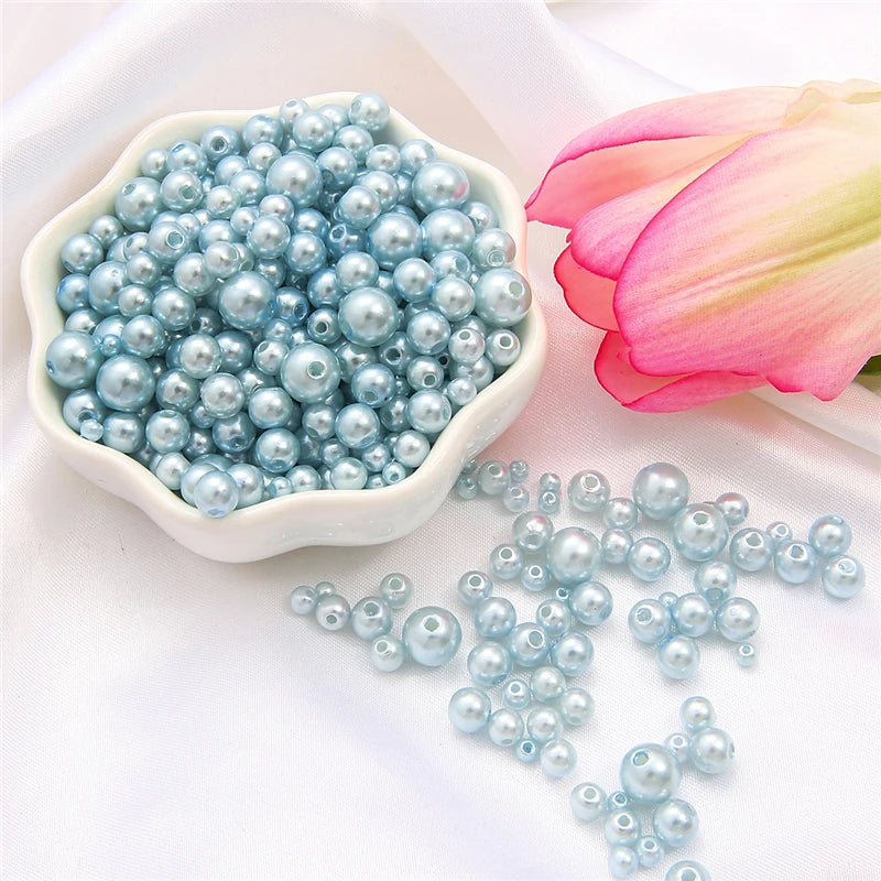 A bowl of light blue pearl beads is shown next to a pink lotus flower on white fabric.