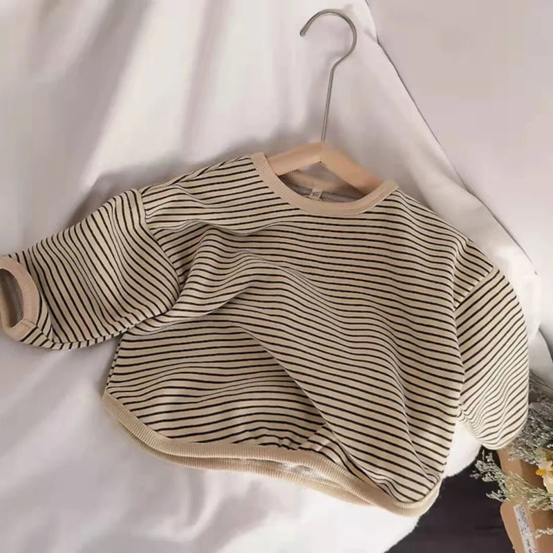 A beige and black striped kids cotton pullover sweatshirt hanging on a wooden hanger against a white background.