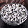 A clear glass bowl filled with small white ceramic beads decorated with black floral patterns.