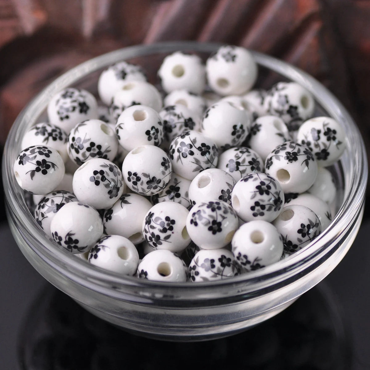 A clear glass bowl filled with small white ceramic beads decorated with black floral patterns.