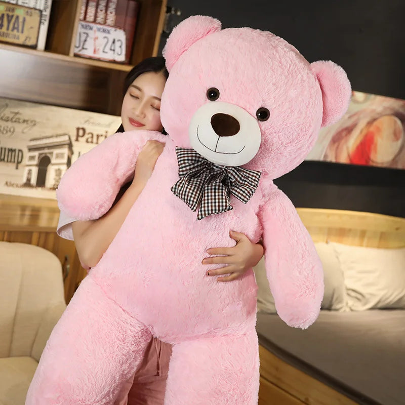 A large pink teddy bear plush toy is being held by a woman in a bedroom setting.